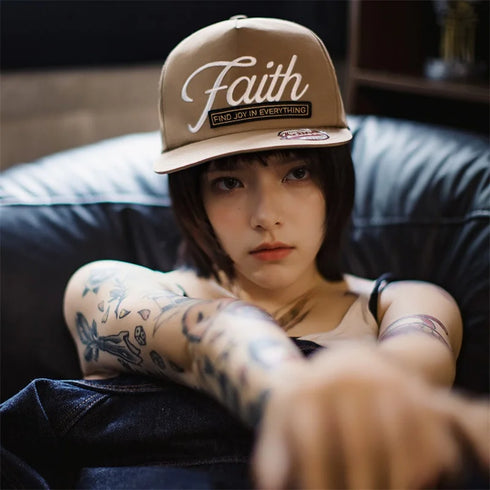 Person wearing a cap with 'Faith' text, sitting on a couch.